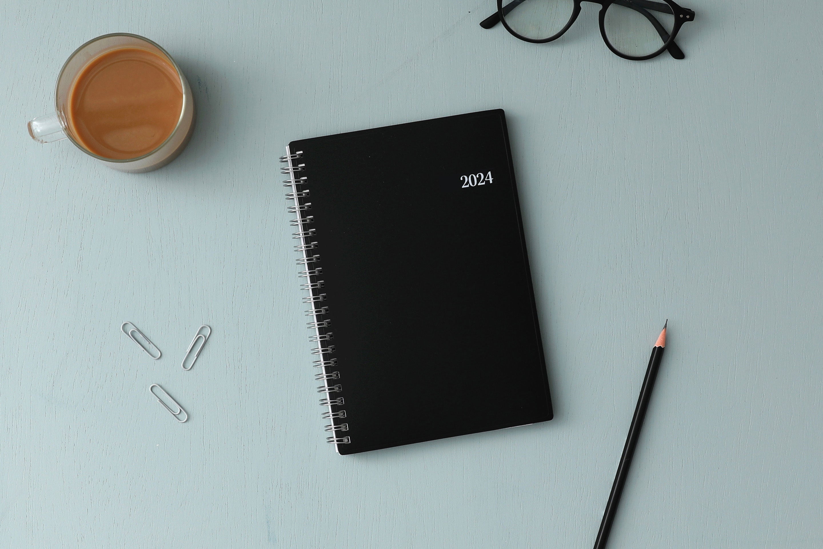Bilingual January 2024 - December 2024 weekly monthly planner featuring a black front cover design and silver twin wire-o binding. calendario de planificacion