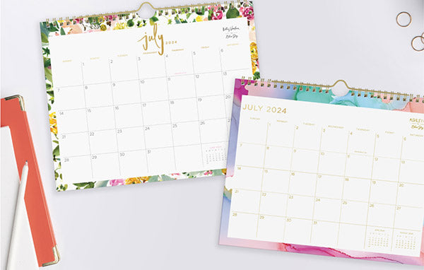 Two vibrant calendars, one adorned with colorful flowers and a pen for jotting down important dates and events.