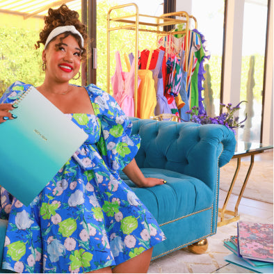 Color Me Courtney brand owner sitting on a blue couch holding a planner from her line