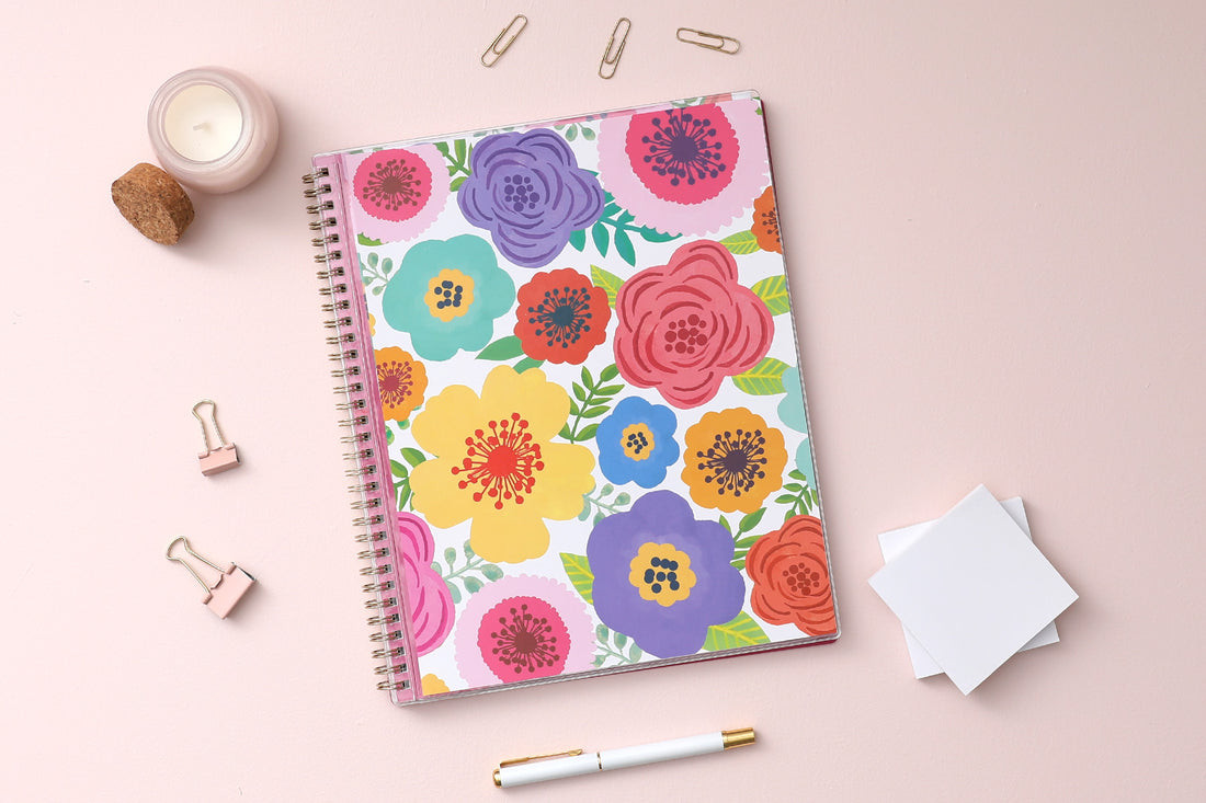 academic weekly monthly planner featuring a floral front cover and twin wire-o binding on lifestyle photo with post-its, pen, paperclips, and candle on the side