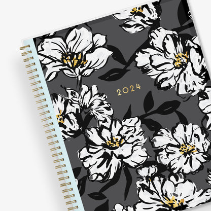 8.5x11 weekly monthly planner for January 2024 - December 2024 new year featuring silver twin wire-o binding, black/gray background, white florals and gold accents