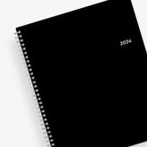 Bilingual January 2024 - December 2024 weekly monthly planner featuring a charcoal front cover design and silver twin wire-o binding 8.5x11 size Calendario De Planificacion.