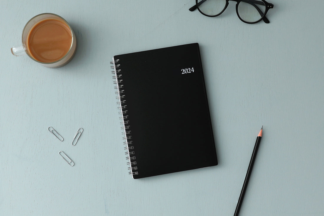 Bilingual January 2024 - December 2024 weekly monthly planner featuring a black front cover design and silver twin wire-o binding. calendario de planificacion