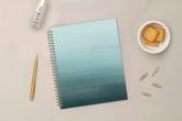 Light blue ocean ombre spiral-bound notebook with gold text on a white background