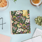 A spiral-bound planner with a dense multicolor floral pattern and a gold &