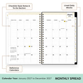 An open spiral-bound planner showing a monthly calendar spread with labeled callouts for checklist style notes and to-do section, lined daily blocks, and reference calendars. The planner page is white with black text and grid lines, plus small beige and yellow accents.