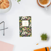 A floral planner calendar cover for 2027 to 2028, featuring a dense multicolor flower pattern on a dark green background with a cream-colored central label. pocket sized monthly planner