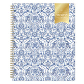 A 2027 weekly monthly planner with a white cover decorated in a blue floral and ornamental pattern, featuring a gold ribbon seal on the top right and a gold spiral binding on the left.