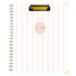 A spiral-bound non-dated planner with a white cover featuring vertical light pink stripes, a gold clip at the top, and a pink oval label in the center with the word &