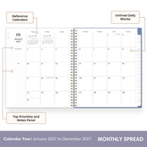 An open spiral-bound planner showing a monthly calendar spread with labeled features including reference calendars, unlined daily blocks, top priorities and notes panel, and a calendar year from January 2027 to December 2027.