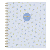 A spiral-bound 2027 agenda with a light blue cover decorated with a delicate pattern of small blue flowers and yellow-green leaves. A circular blue label in the center features the word &