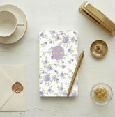 A vertical floral 24 month monthly planner agenda with a white background, decorated with a repeating pattern of light purple roses and green leaves. A lavender oval label in the center reads &