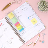 Planner with colorful sticky notes and stationery items on a pink background