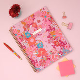 Floral patterned weekly planner with stationery items on a pink background