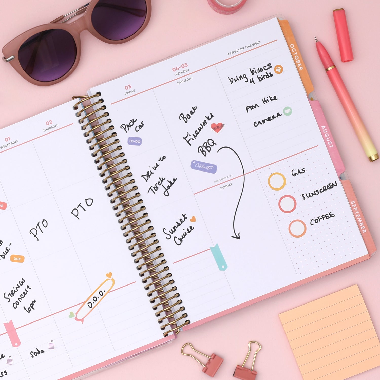Open planner with notes and to-do list on a pink surface with sunglasses, pens, and clips, featuring a weekly spread