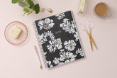 8.5x11 weekly monthly planner for January 2024 - December 2024 new year featuring silver twin wire-o binding, black/gray background, white florals and gold accents