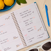 Spiral-bound planner with a to-do list on a table with lemons, a pen, and sunglasses, lined writing space and white monthly tabs