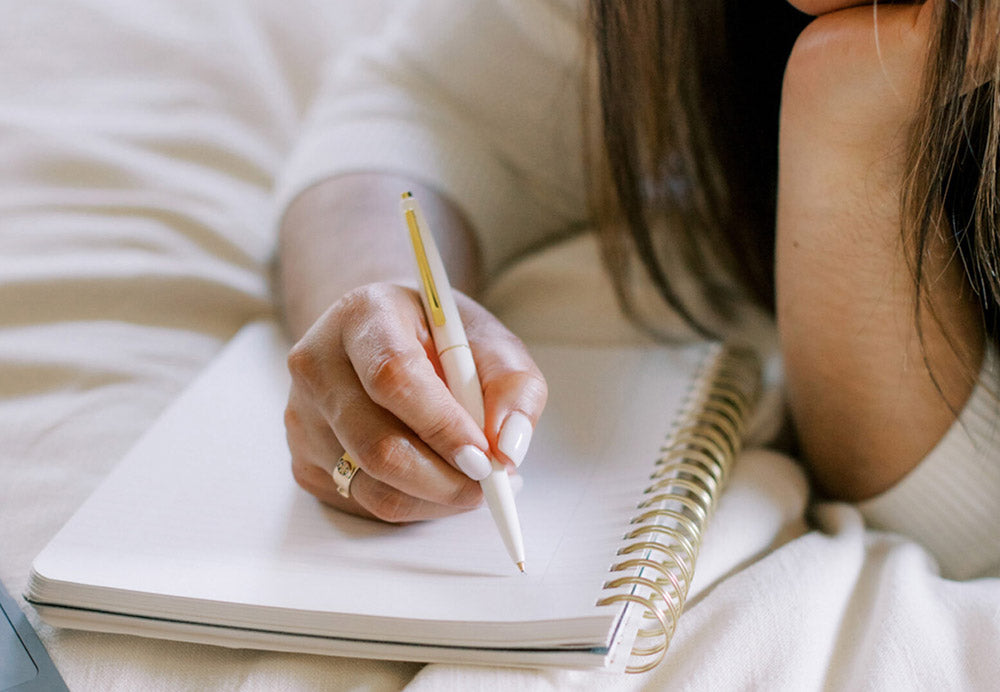 Woman writing in planner with a pen while resting on bed