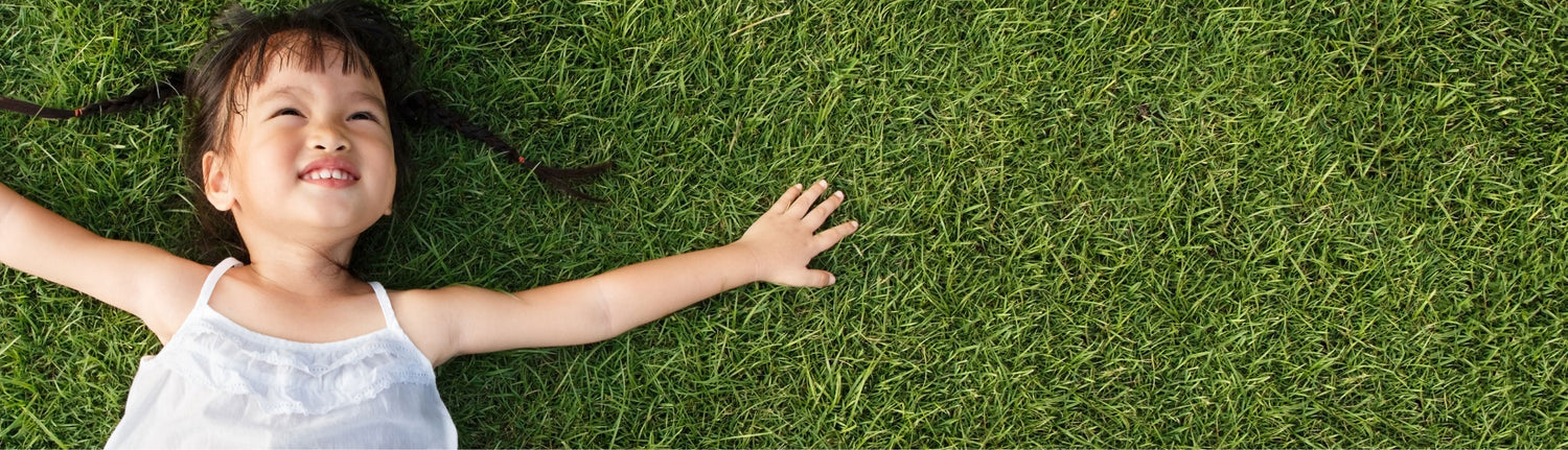 A little girl smiling, laying on a grassy lawn with arms outstretched.