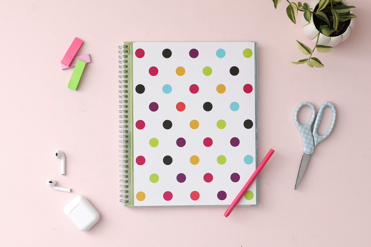 academic teacher lesson planner purple, gold, black, green, and blue dots in 8.5x11 planner size for 2024-2025 academic year. lifestyle photo has pink background, airpods, pink pen, post-its, scissor, and plant.