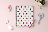 academic teacher lesson planner purple, gold, black, green, and blue dots in 8.5x11 planner size for 2024-2025 academic year. lifestyle photo has pink background, airpods, pink pen, post-its, scissor, and plant.